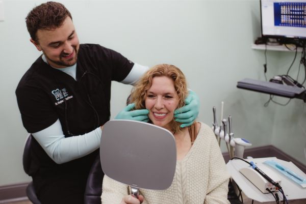 Dr. huffman holding up a mirror up to a patient who's smiling