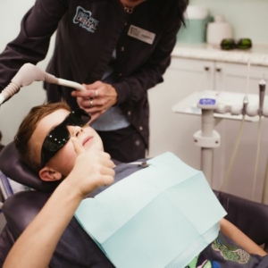 a child leaning back in a dental chair giving a thumbs up to the camera